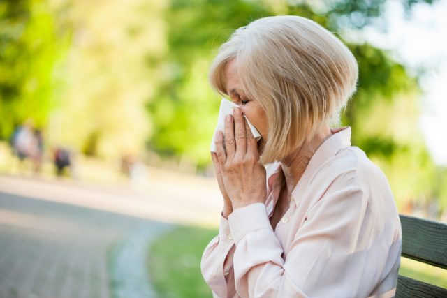 woman sneezing in park