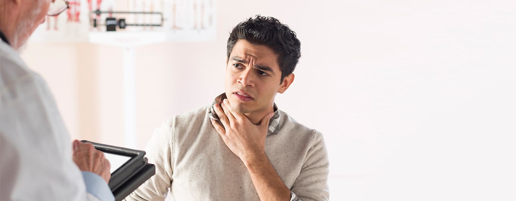 Male patient holding his throat while a doctor evaluates