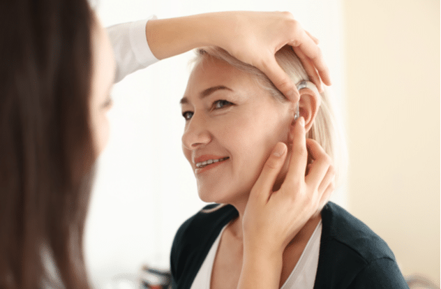 Otolaryngologist putting hearing aid in womans ear on