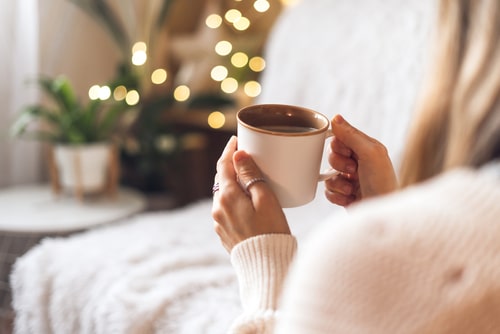 Womans hands in sweater holding cup of hot drink coffee indoors.