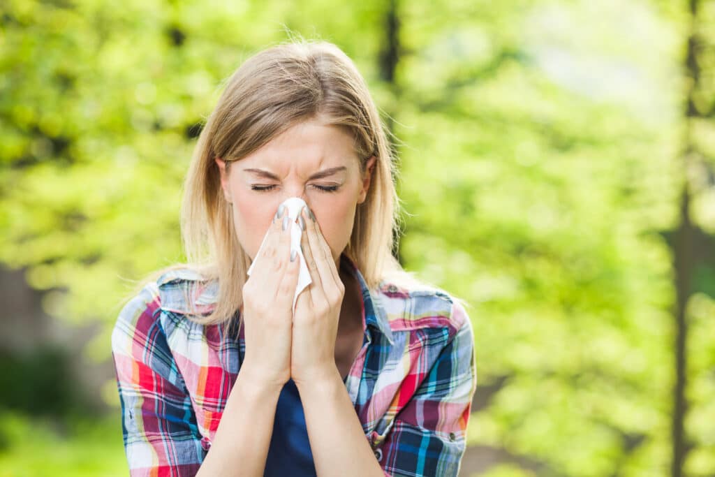 A woman with allergic rhinitis sneezing while standing outdoors